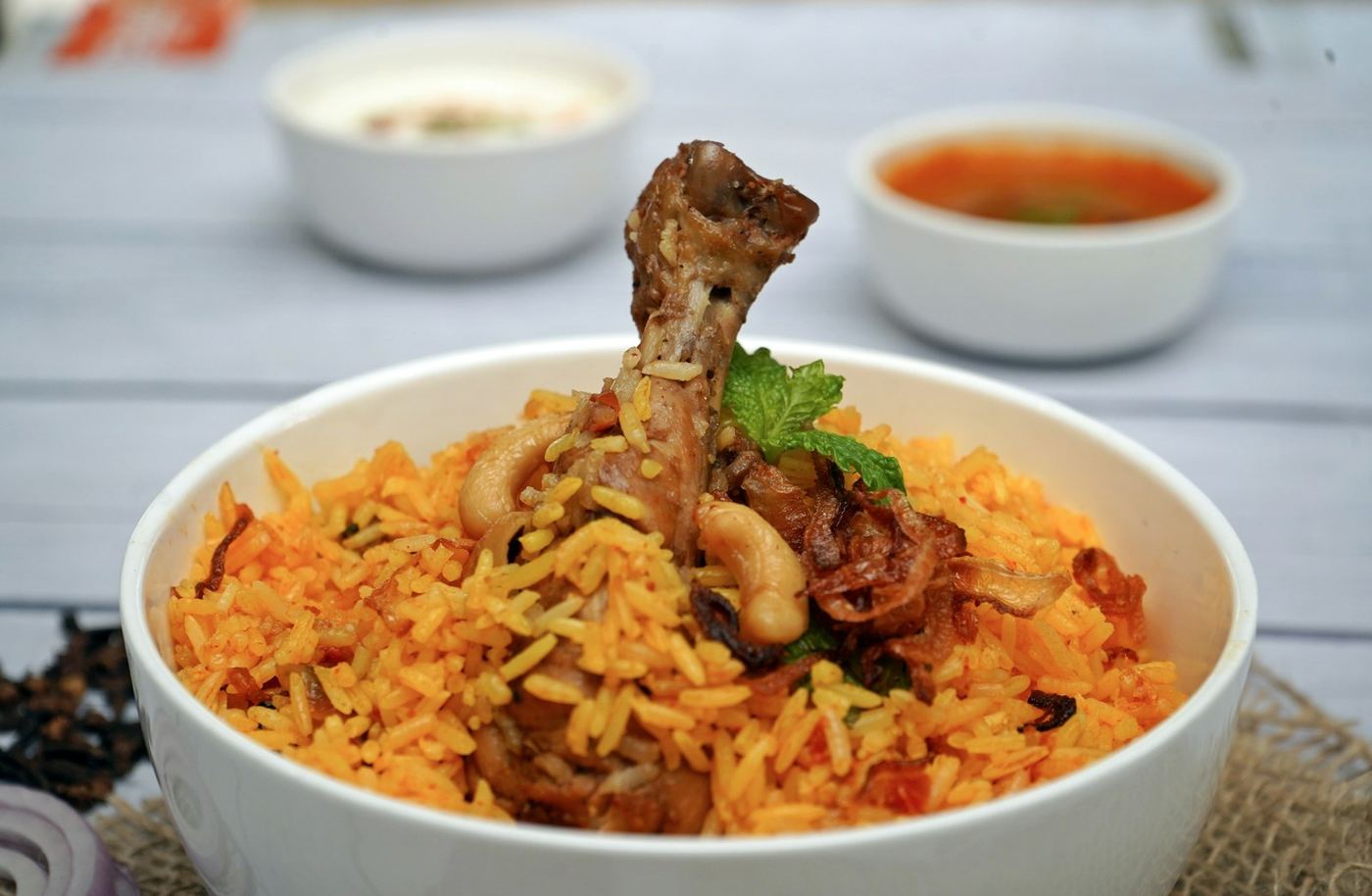 A bowl of biryani with a chicken leg and fried onions